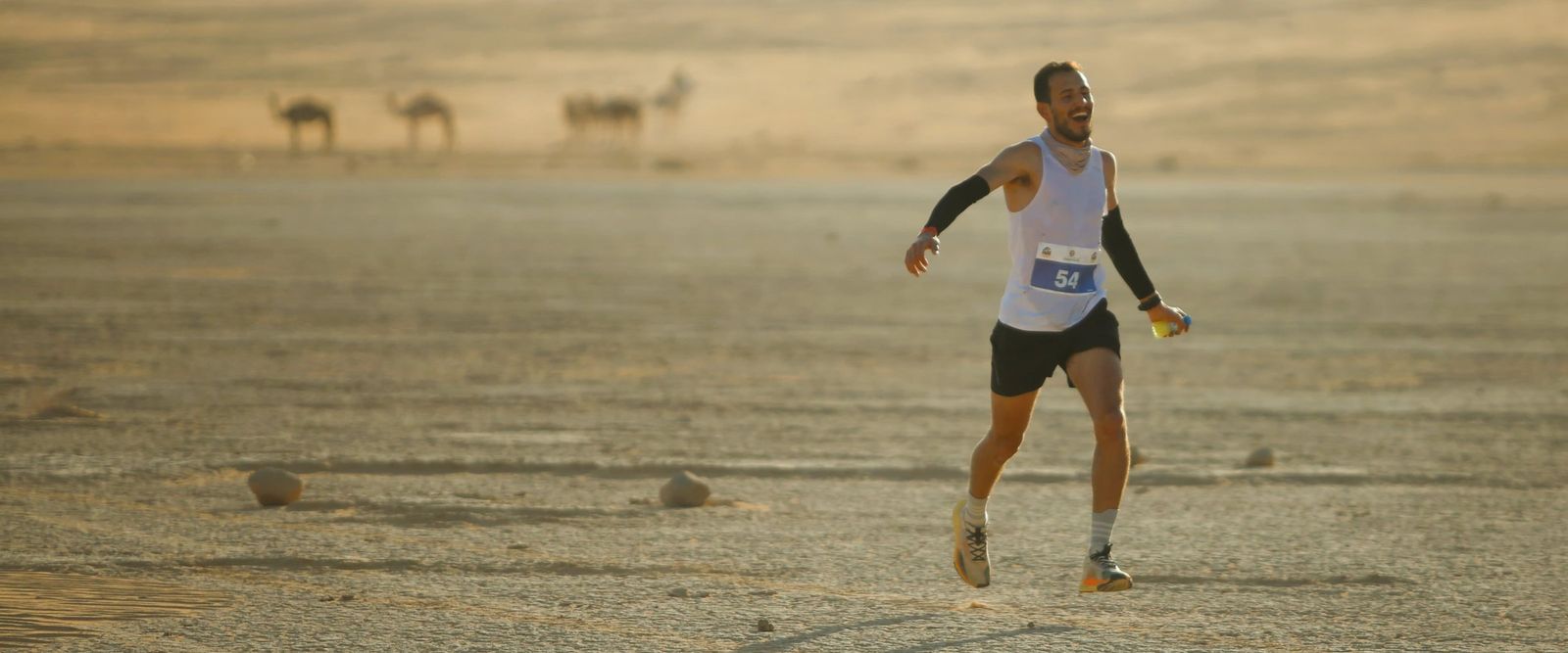 Fuad Abu Safi running across the desert floor at Wadi Rum with camels grazing in the distance